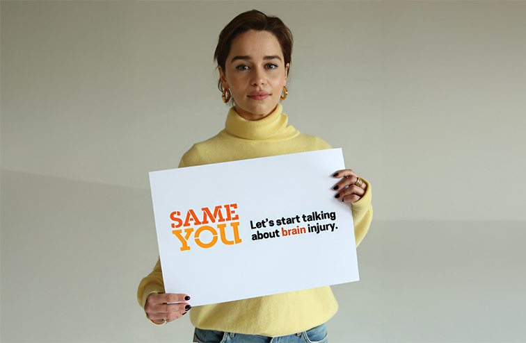 Emilia Clarke holds a sign promoting her brain injury awareness charity, SameYou. 