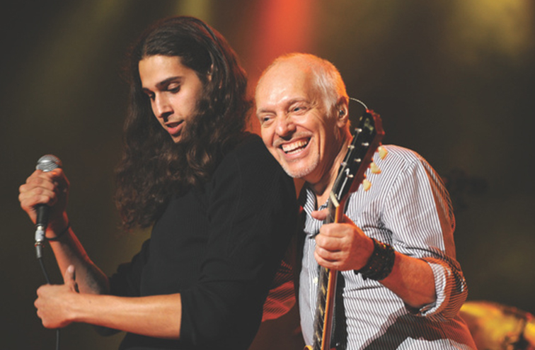 Peter Frampton playing guitar on stage accompanied by his son Julien on vocals in 2019.