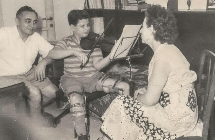 Young Itzhak Perlman, wearing braces as a result of polio, plays violin for his parents.