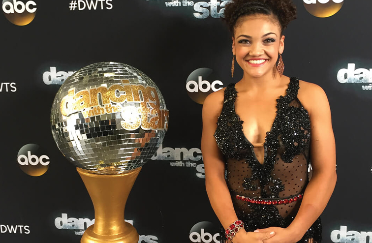 Gymnast Laurie Hernandez in a black sequined dress next to the Dancing with the Stars trophy.