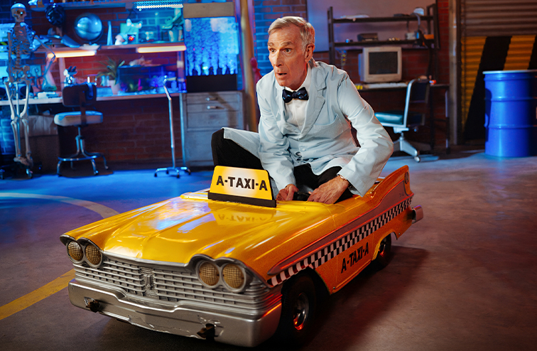 Bill Nye driving a child's taxi toy