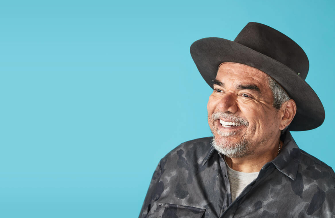 George Lopez smiling, wearing a hat